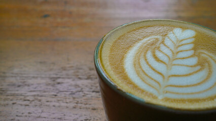 A close-up view of a cup of coffee with intricate latte art in the shape of a leaf