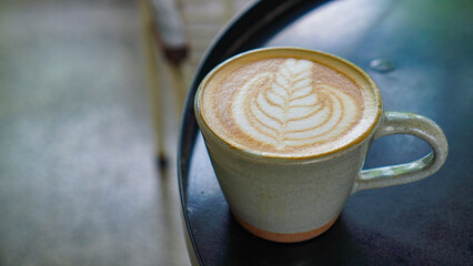 A close-up view of a cup of coffee with intricate latte art in the shape of a leaf