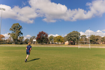 Obraz premium Teenage boy running on empty rugby field towards goal posts