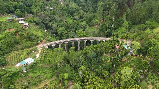 Aerial 4K drone footage of the iconic Nine Arch Bridge near Ella, Sri Lanka. Stunning views of the historic railway viaduct, lush green hills, and scenic train crossing for travel and tourism projects