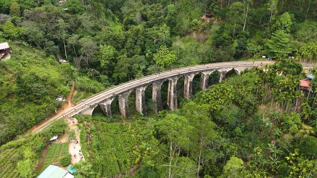Aerial 4K drone footage of the iconic Nine Arch Bridge near Ella, Sri Lanka. Stunning views of the historic railway viaduct, lush green hills, and scenic train crossing for travel and tourism projects