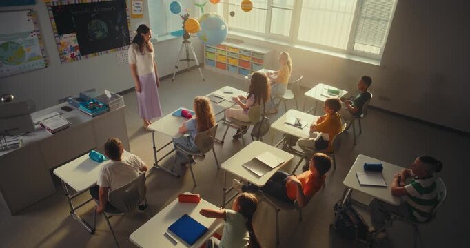 Female Teacher Finishing Lesson, Announcing the End of School Day to Diverse Kids. Elementary School Students Standing Up, Packing Their Backpacks and Leaving Modern School for Holidays. High Angle.