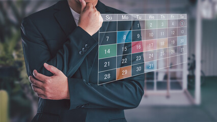 Businessman in suit looking at virtual calendar interface, planning schedule and managing appointments. Concept of business planning, time management, and event organization technology.