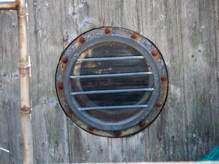 Close-up of a rustic wooden door with a round metal porthole and worn textures, showing age and character.