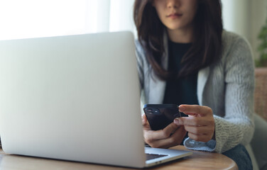 Closeup, business woman using mobile phone during working on laptop computer at coffee shop. Young asian freelancer, entrepreneur using smartphone, online working at home office