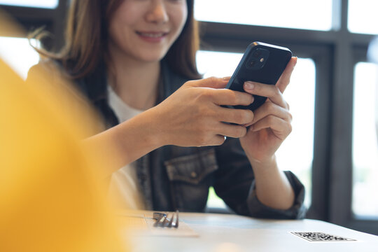 Young asian woman scanning the QR code with mobile phone and order foods at the restaurant. Woman using smartphone for moble banking via mobile app, online payment, close up