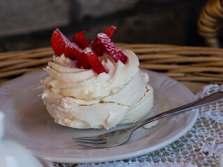 A perfectly crafted Pavlova meringue dessert, adorned with vibrant red strawberries, served on a white plate outdoors.