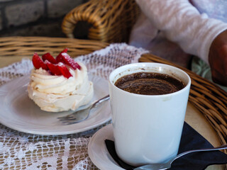 Elegant white meringue cake topped with vibrant red strawberries next to a steaming cup of coffee, set on a lace placemat.