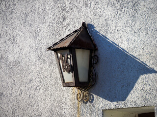 A vintage street lamp with a weathered finish, casting a long shadow on a textured wall, evoking a sense of time.