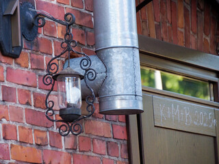 Two old wall lamps with decorative metalwork illuminating a red brick building facade at dusk.