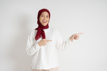 Young woman wearing a red hijab and white top expressing surprise while pointing sideways. Studio shot against a white background, highlighting emotions, cultural attire, and a moment of astonishment.