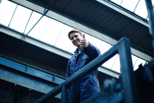 Smiling worker in blue uniform showing thumbs up in factory