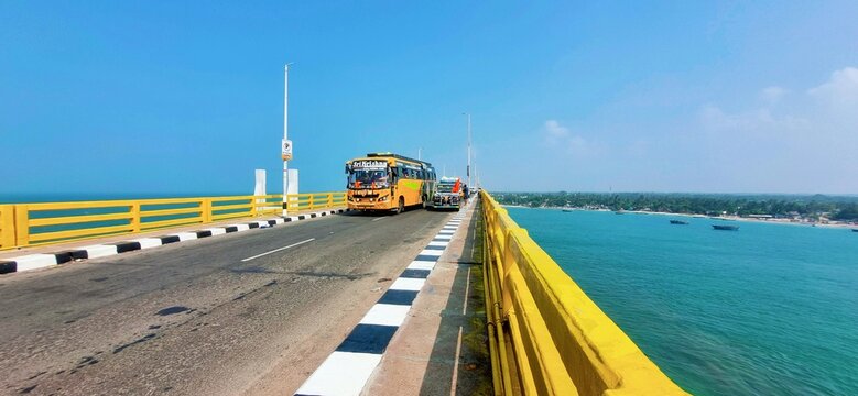 Rameswaram, Tamil Nadu, India &ndash; January 15, 2024: A bright yellow-railed stretch of the Pamban Road Bridge with vehicles crossing over the turquoise waters of the Bay of Bengal under a clear blue sky.