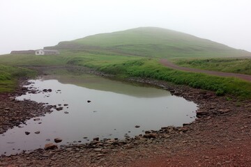 Misty landscape with a small pond reflecting a low hill and a simple building