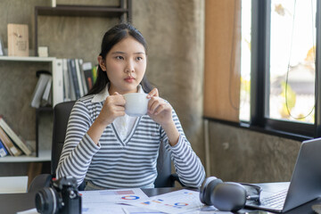A woman is sitting at a desk with a laptop and a cup of coffee