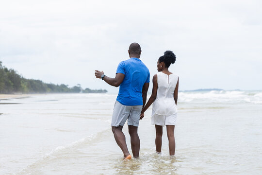 Couple enjoying summer outdoor activities on beach with people walking hand in hand along shore creating peaceful and relaxing atmosphere by water - Powered by Adobe