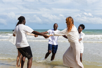 People enjoying summer outdoor activities on beach with people holding hands and playing together near ocean waves under cloudy sky