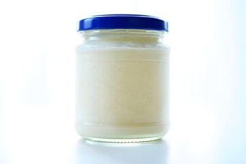 Glass jar filled with creamy white substance and blue lid isolated on white background
