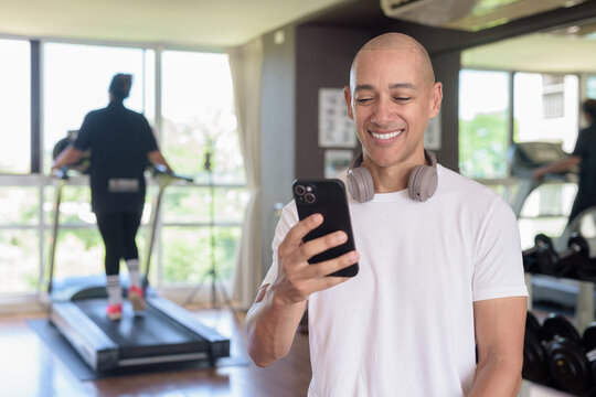 Bald Hispanic man using phone in gym, workout lifestyle, digital fitness and modern training routine