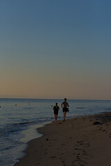 Naklejka premium A young man and woman are seen jogging away from the camera on a sandy beach next to the ocean at sunset.