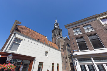 A striking view of a tall Dutch church spire in Gouda rising above historic rooftops and buildings, set against a vast, clear blue sky, capturing the grandeur of a European city.