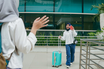 Asian woman in hijab greeting her friend with a warm smile upon arriving at the airport, expressing happiness and excitement
