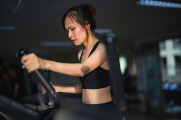 Fototapeta premium A focused woman exercises on a machine in a well-lit gym, showcasing determination and fitness in her workout routine.