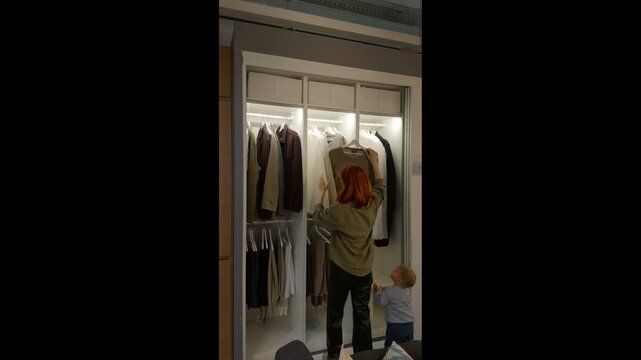 Woman navigates through a furniture store, opening a closet and examining various storage features. She interacts with different furniture displays in a living area setting.
