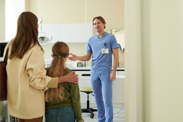 Caucasian male dentist welcoming Caucasian woman and preteen girl into dental office, dentist...