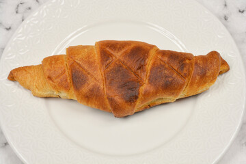 A close-up of a perfectly toasted croissant resting on a white plate with a subtle decorative pattern