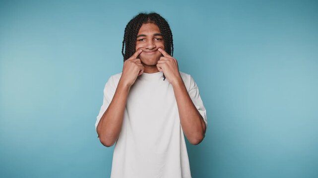 footage of young man poking his cheeks with a playful expression, showing humor and lightheartedness on light blue background