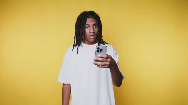 footage of young man with braided hair looks at his phone quizzically on yellow background