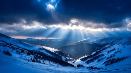 Sunbeams piercing through winter clouds over a snow-capped mountain range.