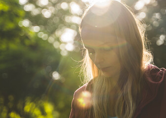 Young woman standing in a sunlit park, enjoying a peaceful moment with soft natural light and sun flares around her