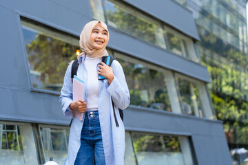 A young woman wearing a blue shirt and a white shirt is holding a cell phone and a book. She is smiling and she is happy