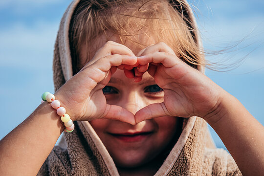Girl makes heart shape with hands by the sea