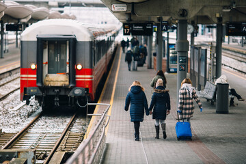 Travelers Walking Along a Busy Train Station Platform with Bright Blue Suitcase on a Chilly Day
