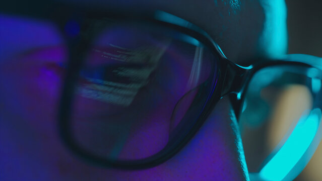 Programmer working late at night wearing glasses reflecting code