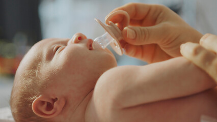 Mother giving pacifier to newborn baby lying on back