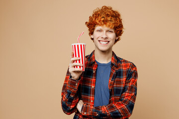 Young redhead man he wear red shirt blue t-shirt casual clothes hold in hand cup of soda pop drink cola water isolated on plain pastel light beige background studio portrait. Lifestyle concept