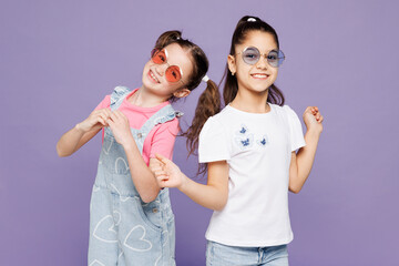 Little two smiling cheerful cool friends kids children girls 9-10 years old wear casual clothes sunglasses together point have fun look camera isolated on plain purple background. Lifestyle concept.