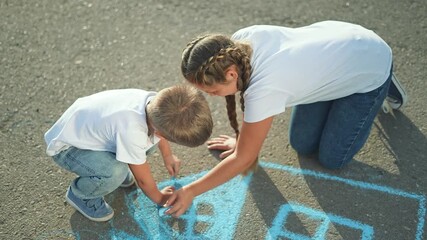 Children drawing house chalk on street. Siblings enjoy outdoor creativity, drawing house together. Fun childhood moments as children draw on street with chalk. Kids express imagination drawing house.