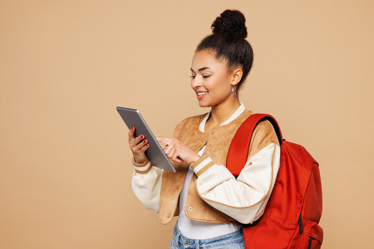 Young smiling happy smart girl IT student wears casual clothes backpack bag hold use digital tablet pc computer isolated on plain pastel light beige background. High school university college concept.