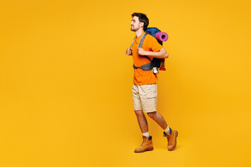 Full body young traveler man carry backpack with stuff mat walk go isolated on plain yellow background. Tourist leads active healthy lifestyle walk on spare time. Hiking trek rest travel trip concept.