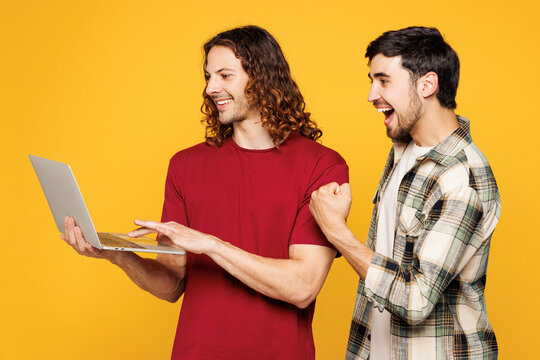Young happy two friends buddies IT men wear casual clothes together hold use work on laptop pc computer do winner gesture isolated on plain yellow orange background studio portrait. Lifestyle concept.