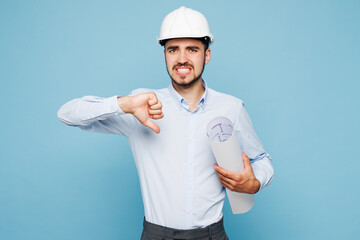 Young architect engineer designer employee man wear white clothes shirt hardhat hold blueprints show thumb down dislike gesture isolated on plain blue background studio portrait Work on build project