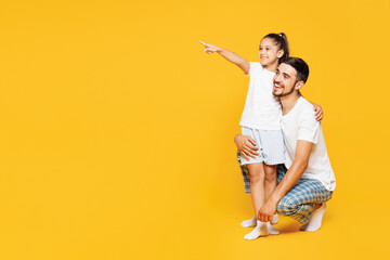 Full body young parent man with child girl wear casual blue pyjamas clothes. Daddy little kid point index finger aside on area sit isolated on plain yellow background Father's Day Love family concept