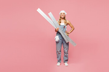 Full body young happy employee laborer handyman woman wear denim overhaul hold in hand metal profile isolated on plain pink background. Instruments for renovation apartment room. Repair home concept.