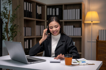 woman is talking on her cell phone while sitting at a desk with a laptop