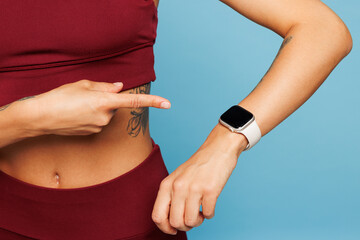 Close up cropped young fitness trainer instructor sporty woman sportsman wear red sportswear blank screen smart watch train in home gym isolated on plain blue background Workout sport fit abs concept